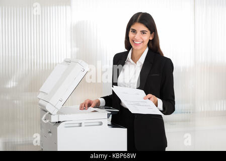 Junge Geschäftsfrau mit Kopierer im Büro Stockfoto