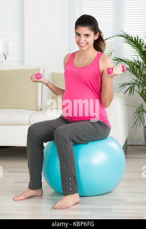 Portrait von glücklichen schwangeren Frau Hanteln beim Sitzen auf Fitness Ball zu Hause Stockfoto