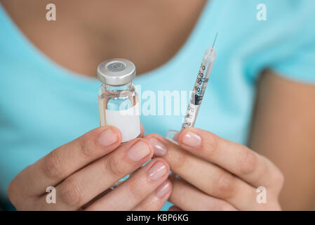 Mittelteil der jungen Frau mit Medizin Flasche und Spritze zu Hause Stockfoto