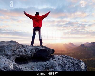 Die Zahl der Männer in rot Outdoor Jacke an scharfen Klippe. Berge im frühen Herbst Daybreak. Konzeptionelle Szene. Stockfoto