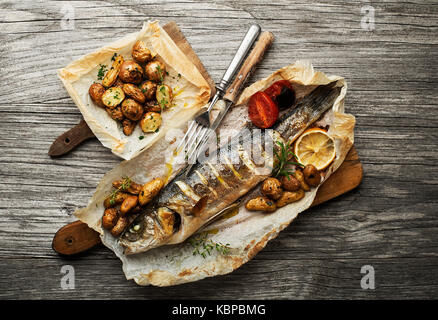 Gebackener Wolfsbarsch mit Bratkartoffeln auf hölzernen Tisch Stockfoto