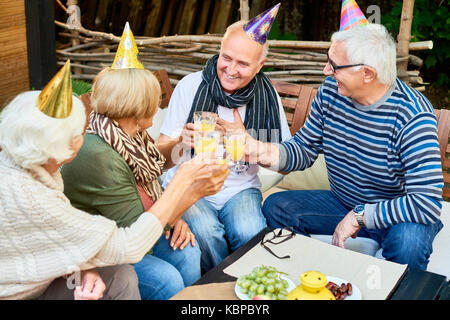 Portrait von lächelnden älteren Mann, der Partei hat das Toasten mit einer Gruppe von Freunden seinen Geburtstag im Café im Freien feiern. Stockfoto