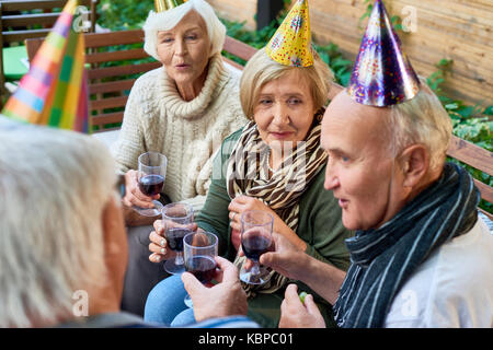 Gruppe der älteren Freunde tragen warme Kleidung, Brille mit roten Jammern in den Händen und plaudern miteinander, während mit Outdoor Party Stockfoto