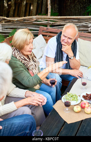 Profil anzeigen von der hübschen alten Frau hält Glas roten Wein in der Hand beim unterhalten Ihre Gäste mit Small Talk, Sie genießen die Atmosphäre von Bac Stockfoto