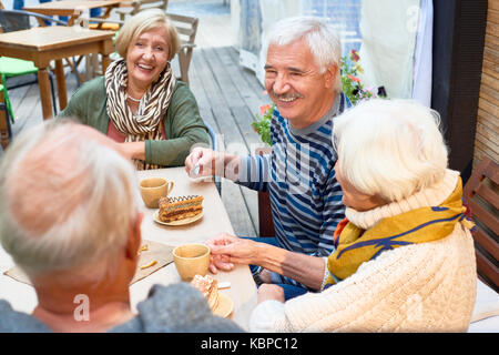Freudige ältere Freunde in Tea Party im schönen Café im Freien: Sie genießen Sie Kuchen und duftenden Kaffee und unterhalten sich angeregt miteinander Stockfoto