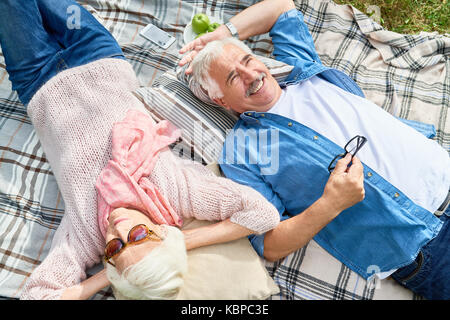 Hohe Betrachtungswinkel und der liebevollen Älteres Paar beim jede andere Firma, während auf der gemütlichen Plaid bei Sunny Green Park ruhenden Stockfoto