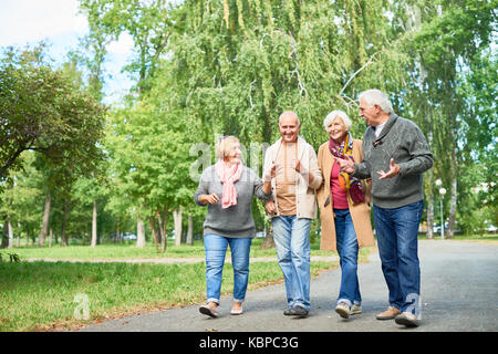 Fröhliche Gruppe von älteren Freunden tragen warme Kleidung entlang Park Alley und unterhalten sich angeregt miteinander, malerischen Blick auf Hintergrund Stockfoto