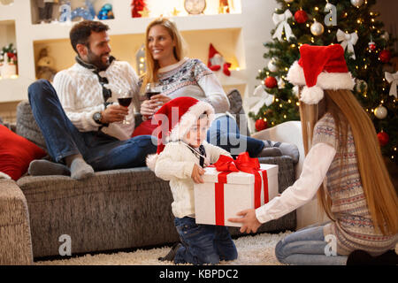Glückliche Kinder mit Weihnachtsgeschenk genießen mit den Eltern Heiligabend Stockfoto
