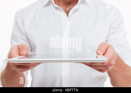 Zugeschnittenes Bild des jungen Mannes stehen über weiße Wand Hintergrund isoliert. Geben Sie einen Tablet-PC. Stockfoto