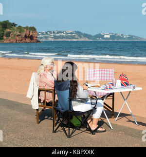 Eine Mutter und Tochter entspannen durch den Sand ausserhalb ihrer Hütte am Strand Goodrington Sands, Paignton genießt eine sehr britische Marke Tasse Tee. Stockfoto