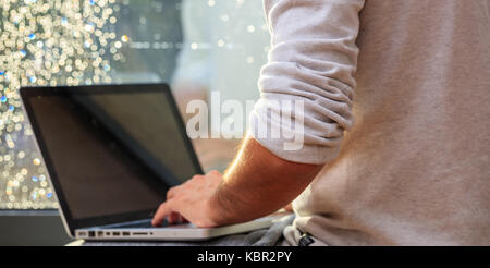 Junge Mann sitzt vor einem Fenster, die Arbeit mit einem Laptop Stockfoto