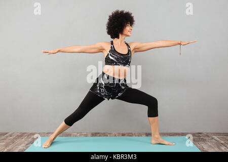 Bild der hübschen lockigen fitness Frau, sport Yoga Übungen über graue Wand. Neben der Suche. Stockfoto