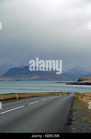 Ein Blick auf einer menschenleeren Straße um Hvalfjordur, Isländisch mit Bergen in der Ferne. Under A Dark Sky auf einem sehr bewölkten Tag gesehen. Stockfoto