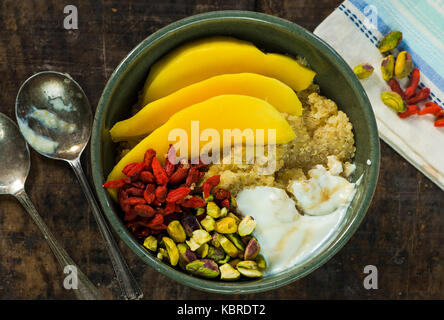 Quinoa Porridge mit Mango, Pistazien, Goji Beeren und Honig Joghurt - Ansicht von oben. Gesundes Frühstück option. Stockfoto