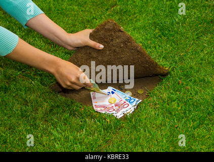 Finanzen Konzept, Hände Geld versteckt sich unter dem Gras Stockfoto