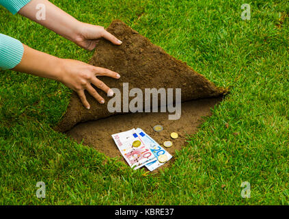 Finanzen Konzept, Hände Geld versteckt sich unter dem Gras Stockfoto