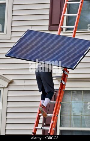 Solar Panel Techniker mit Solarmodulen bis Leiter auf das Dach eines Hauses Stockfoto