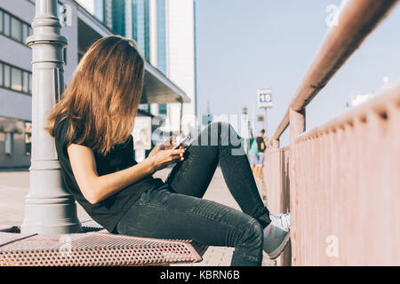 Schlanke Mädchen mit braunem Haar verwendet ein Mobiltelefon in der Stadt Stockfoto