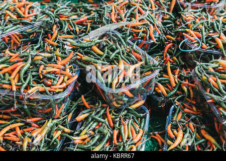 Grüne und rote Chilis in Kunststoffbehältern auf Verkauf zu einem Straßenmarkt Stockfoto