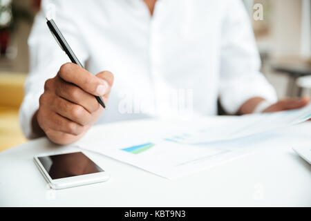 7/8 Image der jungen afrikanischen Mann sitzt Coworking holding Dokumente. Stockfoto