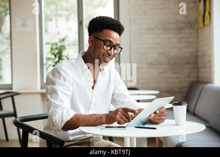 Bild der glücklichen jungen afrikanischen Mann sitzt Coworking mit Tablet-PC. Neben der Suche. Stockfoto
