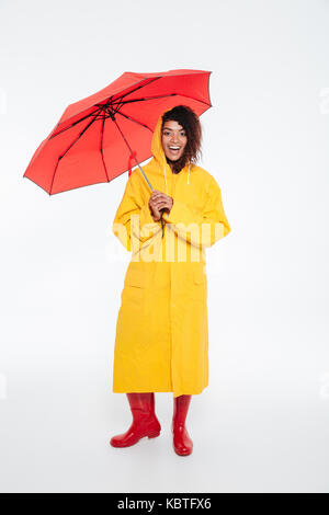 Volle Länge Bild der afrikanischen Frau gerne in Regenmantel Posiert mit Regenschirm, und wenn man die Kamera auf weißem Hintergrund Stockfoto