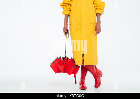 Zugeschnittenes Bild der afrikanischen Frau in Regenmantel mit Regenschirm auf weißem Hintergrund Stockfoto