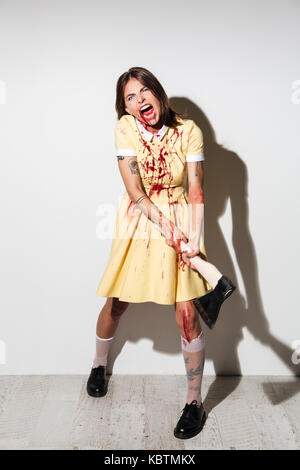 Die ganze Länge der Ein unheimlich zombie Mädchen mit Blutflecken bereit, mit einer großen Axt auf weißem Hintergrund in Angriff abgedeckt Stockfoto