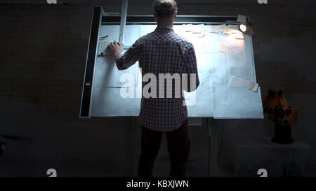 Junge Ingenieur, der an der Tafel mit Zeichnung und Plan anzeigen. Männliche Architekt am Reißbrett und Grundriss mit Bleistift in der Hand im Büro Stockfoto