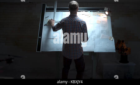 Junge Ingenieur, der an der Tafel mit Zeichnung und Plan anzeigen. Männliche Architekt am Reißbrett und Grundriss mit Bleistift in der Hand im Büro Stockfoto