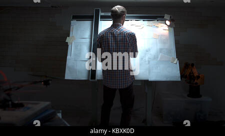 Junge Ingenieur, der an der Tafel mit Zeichnung und Plan anzeigen. Männliche Architekt am Reißbrett und Grundriss mit Bleistift in der Hand im Büro Stockfoto