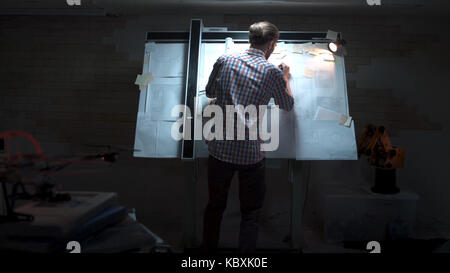 Junge Ingenieur, der an der Tafel mit Zeichnung und Plan anzeigen. Männliche Architekt am Reißbrett und Grundriss mit Bleistift in der Hand im Büro Stockfoto