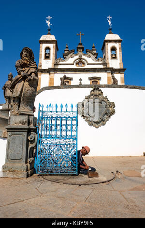 Obdachlosen vor den Toren von Wallfahrtskirche Bom Jesus tun, Matosinhos, Speckstein Statue des Propheten Jesaja, die von Aleijadinho, Congonhas, Minas Gerais, Brasilien. Stockfoto