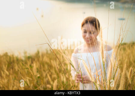 Asiatische Mädchen auf einer grünen und gelben Gras Feld holding Gras in ihrer Hand, Phuket, Thailand Stockfoto