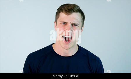 Ein junger Mann schreit die kamera mit schwarzem T-Shirt und grauer Hintergrund Stockfoto