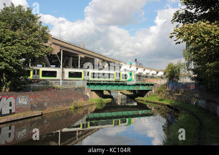 Eine London Midland Zug spiegelt sich im Wasser wie es kreuzt ein Kanal bei Spon Lane in der Nähe von smethwick unter M 5 Oldbury Viadukt in das Schwarze Land. Stockfoto