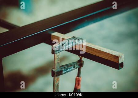 Handwerker mit Schraubzwingen fixieren zwei Stücke Holz und Eisen. Der Prozess, Schreibtisch, Möbel Stockfoto