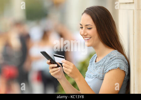 Happy girl Bezahlung Online mit Kreditkarte und einer Smart Phone lehnte sich an eine Wand auf der Straße Stockfoto