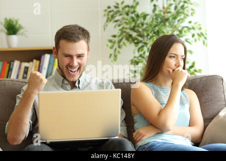Luddite Mann auf der Linie mit einem Laptop seine traurigen Frau auf der Couch zu Hause sitzen ignorieren Wetten Stockfoto
