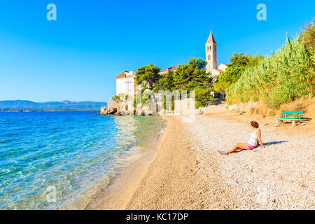 Junge Frau Touristen sitzen am Strand mit Blick auf die Dominikanische Kloster in Bol, Insel Brac, Kroatien Stockfoto