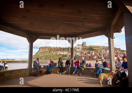 Der Verzehr von Fisch und Chips und/oder Eis im musikpavillon am schottischen Kopf neben dem Hafen, mit Whitby Abbey Hinter, North Yorkshire, England Stockfoto