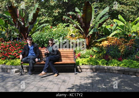 Zwei Personen sitzen auf einer Bank in einem Park mit Gärten im Hintergrund Stockfoto