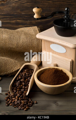 Kaffeebohnen in Holz- Schaufel und gemahlenen Kaffee in Houten mit Kaffee Mahlwerk auf dunklen Holztisch Hintergrund Stockfoto