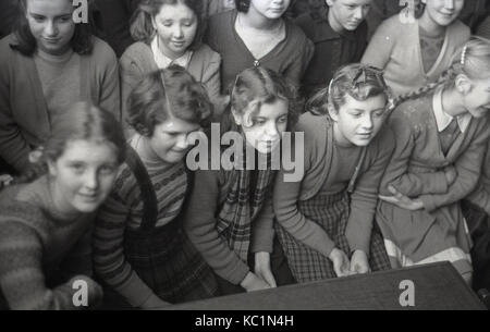 1948, historische, post-ww2 Großbritannien mit Lebensmitteln Rationierung, hier sehen wir Englisch Schule Mädchen sitzen gemeinsam in einer Schule Halle wartet ein Lebensmittel Paket (Geschenk) an die Schule, die der Ausschuß der Australischen Geschenk Paket Regelung zu erhalten. Stockfoto