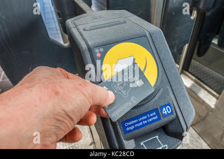U-Bahnhof-man's Hand mit einer Bankkarte (Namen und Nummern geändert) auf eine kontaktlose Zahlung Leser, auf eine Barriere. England, UK. Stockfoto