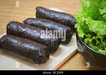 Japanische Küche, Traditionelle ungeschnitten Japanischen Reis Maki Sushi Roll mit Nori Algen auf Schneidebrett serviert mit grünen Eichen. Stockfoto