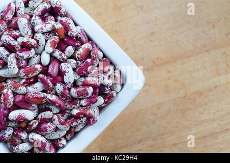 Bean Sorten Schlucken Rot und Weiß mit Punkten in einem weißen Keramik Schüssel auf einem hölzernen Hintergrund. Ansicht von oben. Stockfoto