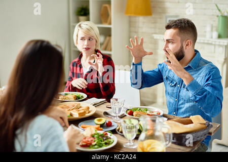 Porträt der jungen Freunde genießen das Abendessen zusammen und großen festlichen Tisch und Geschichten aktiv Gestik im lebhaften Gespräch Stockfoto
