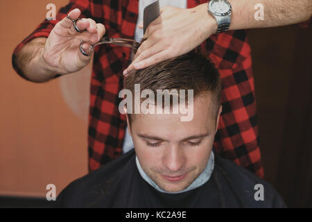 Kaukasische junger Mann im Barbershop. Barber ist cuttinhg sein Haar in hipster Style. Stockfoto