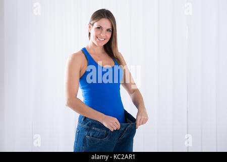 Glückliche junge Frau zeigt Ihre Weightloss durch das Tragen von alten Jeans Stockfoto